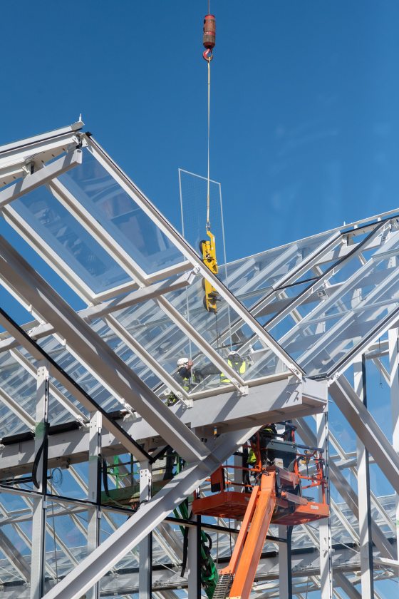 a piece of glass hanging from a crane being installed on steel beams